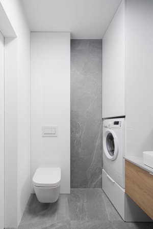 Simple bathroom with white furniture and walls, washing machine and toilet and gray wall and floor tilesの写真素材
