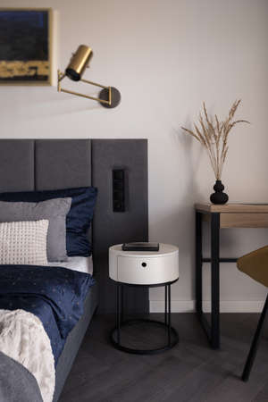 Stylish bedside table in functional bedroom with comfortable bed and desk with chair to workの写真素材