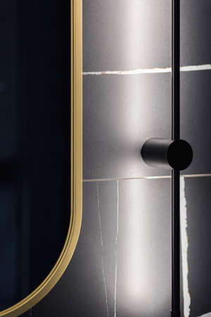 Close-up on modern, black led light lamp on wall with marble tile next to oval mirror in golden frameの写真素材