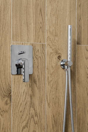 Close-up on modern silver shower tap mounted in wall with wooden style tilesの写真素材