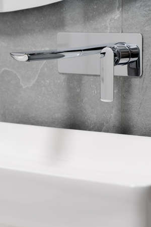 Stylish silver, chrome tap in wall with gray tiles over white, bathroom sinkの写真素材
