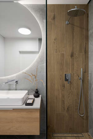 Modern shower cabin with wooden style tiles next to stylish washbasin under big, round mirrorの写真素材