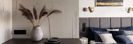 Panorama of small and stylish table with decorations next to bedroom area with cozy bedの写真素材