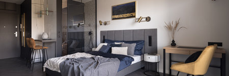 Panorama of modern, open plan studio apartment with bedroom with desk next to shower behind glass wallの写真素材