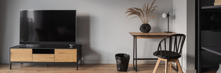 Panorama of small home office with wooden desk, stylish decoration and chair next to big tv on wooden sideboard in living roomの写真素材