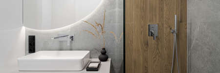 Panorama of modern and small bathroom with wooden style tiles in shower cabin next to round mirror with led light above washbasinの写真素材