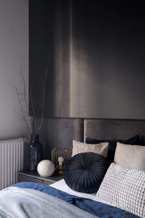 Dark and elegant bedroom corner with cozy bed with nice bedclothes and stylish bedside table with modern decorationsの写真素材