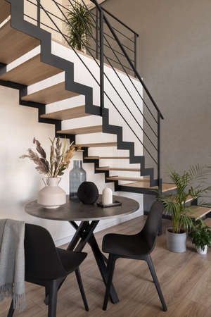 Small, round dining table with two chairs under wooden stairsの写真素材