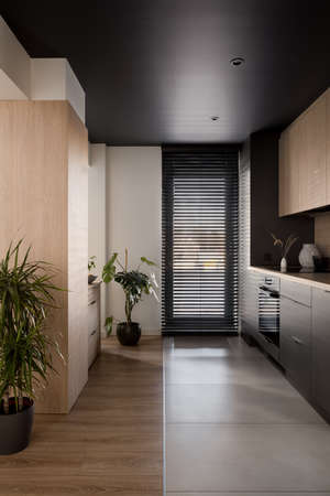 Modern kitchen with black ceiling, wooden furniture and big window with black blindsの写真素材