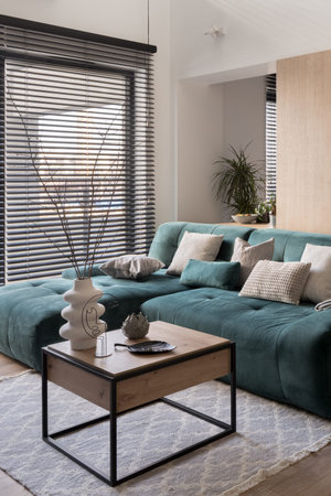 Square, wooden coffee table with decorations and cozy green couch in living room with big window...