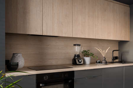 Small kitchen with wooden and gray furniture, black oven and induction hob and black tapの写真素材