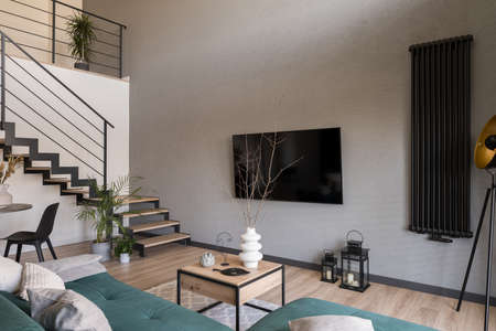 Big tv on concrete wall in modern living room with stylish furniture and decorations and wooden stairsの写真素材