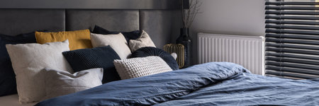 Panorama of comfortable bed with stylish bedclothes and many pillows in small bedroom