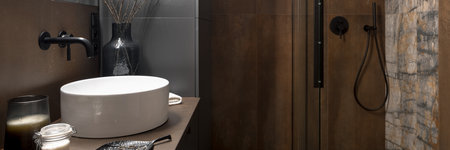 Panorama of trendy bathroom with small white washbasin, black tap, stylish decorations and showerの写真素材