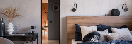 Panorama of elegant bedroom with cozy bed with wooden headboard, mirror in black frame and decorated deskの写真素材
