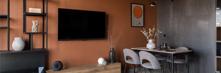 Panorama of decorated table with gray chairs in room with tv on stylish orange wallの写真素材
