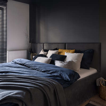 Big and cozy bed in modern and dark bedroom with gray wall and headboardの写真素材