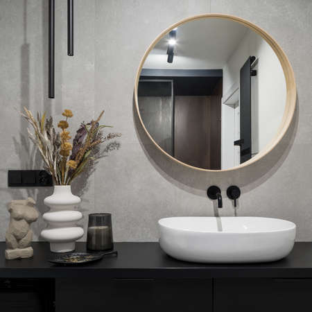 Stylish decorations, big round mirror over oval, white washbasin in simple, black cabinet in modern bathroom with concrete wallの写真素材
