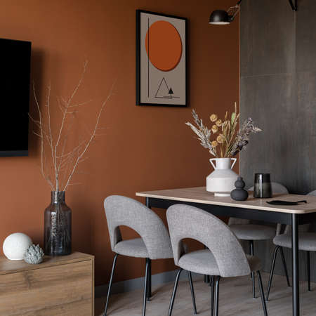 Orange wall in stylish dining room with simple table, elegant gray chairs and decorationsの写真素材