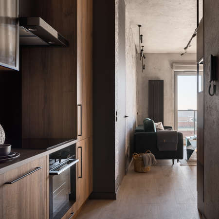 Small kitchen with wooden furniture in corridor open to living room with sofaの写真素材