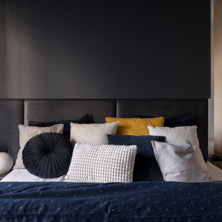 Close-up on comfortable bed with headboard and many decorative pillows in modern dark bedroomの写真素材