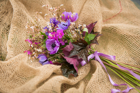Garden style summer bouquet. Mix of lilac and purple anemone flowers, geranium flowers and heuchera or alumroot leaves. Bouquet on sackcloth background. Garden style wedding bouquet. Flower design.の写真素材