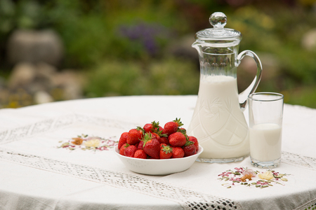Bowl of strawberries standing on the table with glass of milk. Jug full of milk beside bowl of strawberries. Summer breakfast. Summer desert. Picnic idea. Healthy optionの写真素材