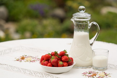 Bowl of strawberries standing on the table with glass of milk. Jug full of milk beside bowl of strawberries. Summer breakfast. Summer desert. Picnic idea. Healthy optionの写真素材