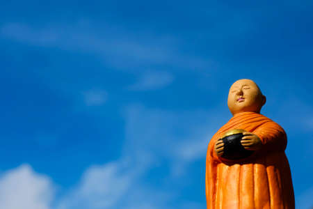 Buddhist Monk is standing with blue sky background, ceramic monk.の写真素材