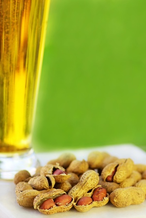 glass of cold beer with peanuts ongreen background の写真素材