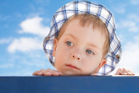 sad  little boy in hat looking away on sky background の写真素材