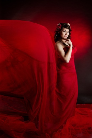 Beautiful woman in red waving flying dress. Smiling and looking at camera. Low keyの写真素材