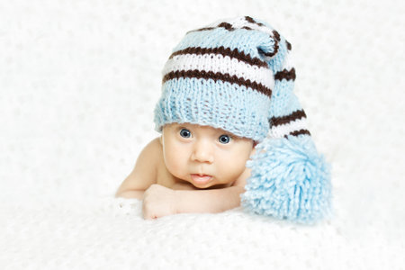 Newborn baby closeup portrait in blue woolen hat over white soft background. Indigo eyes
