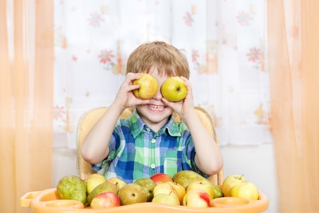 Happy boy playing with apples in front of the table with fruits. Indoors portraitの写真素材