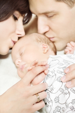 Parents with newborn baby lying down and kissing child  Family and parenting conceptの写真素材