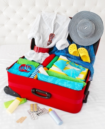 Travel suitcase packed for vacation with personal belongings. Concept. Preparation for holidays in sea resort: what to pack to the luggage. Isolated on whiteの写真素材