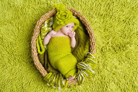 Newborn baby in woolen hat inside basket over green backgroundの写真素材