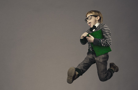 child running back to school, funny kid portrait, jumping smart schoolboy with glasses and bookの写真素材