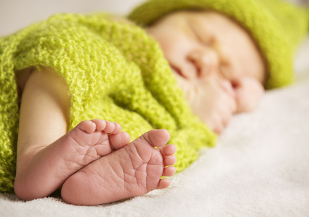 Newborn Baby Feet, New Born Child Sleeping, Kid Foot Covered by Green Knitted Wool Clothの写真素材