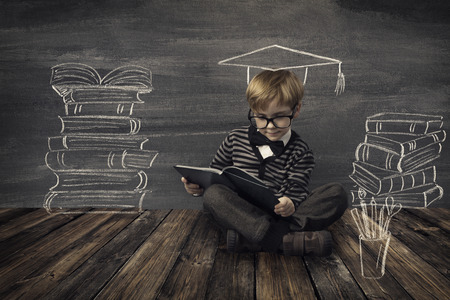 Child Little Boy in Glasses Reading Book over School Black Board with Chalk Drawing, Kids Preschool Development, Children Education Conceptの写真素材