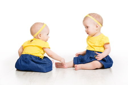 Babies Girls Twins, Two Kids Sitting on Floor, Children Sisters Portrait, Isolated over White Backgroundの写真素材