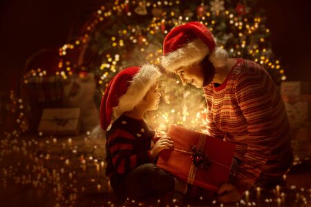 Family open Christmas Lighting Present Gift Box front of Xmas Tree, Happy Mother with Baby Child in Magic Nightの写真素材