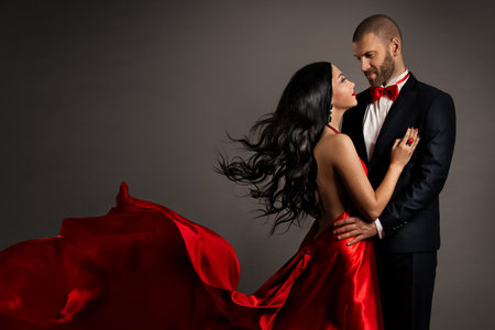Lovely Happy Couple dancing. Woman in red Dress and Man in Black Suit with Bow Tie. Flying silk Fabric and hair on Wind. Studio Backgroundの写真素材