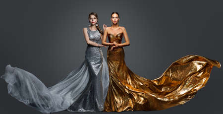 Fashionable two Woman in Golden Evening Dress and Silver Gown. Glamour Beauty Model Fashion Prom Clothes with Train. Studioの写真素材