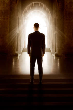 Man Back View Silhouette in Window Door Light.  Groom in Black Suit Standing Dark Mystery Church Aisleの写真素材