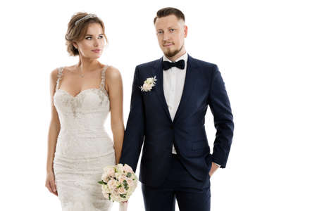 Wedding Couple Fashion Portrait. Bride in Lace Dress and Groom in Classic Suit with Flowers Bouquet over Isolated White Studio Backgroundの写真素材