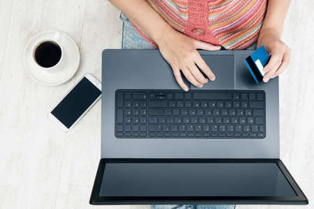 Woman Hand holding Credit Card and using Laptop making Online Payment. Top View of Hands work with Computer and Bank Card. Online Shop and Bank at Homeの写真素材