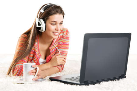 Smiling Woman use Laptop in Headphone. Young Girl work on Computer at Home. Happy Student Study in Earphone lying down and looking at Notebook Screen over White Backgroundの写真素材