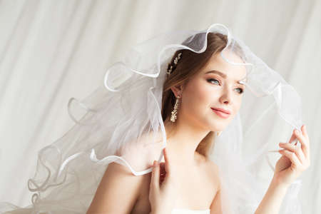 Bride in Veil. Wedding Make up and Bridal Hairstyle Fashion Portrait. Romantic Bride Looking Away at Window and Dreaming. Beauty Wedding Woman Face Close up over Whiteの写真素材