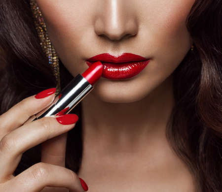 Beauty Model applying Red Lipstick. Perfect Lips Make up and Nail Polish Close up. Glamour Face Makeup Cosmeticsの写真素材